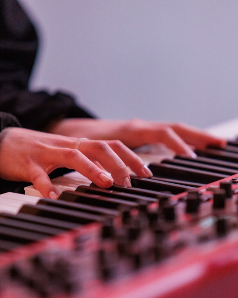Close-up of hands playing red electronic keyboard during musical performance.