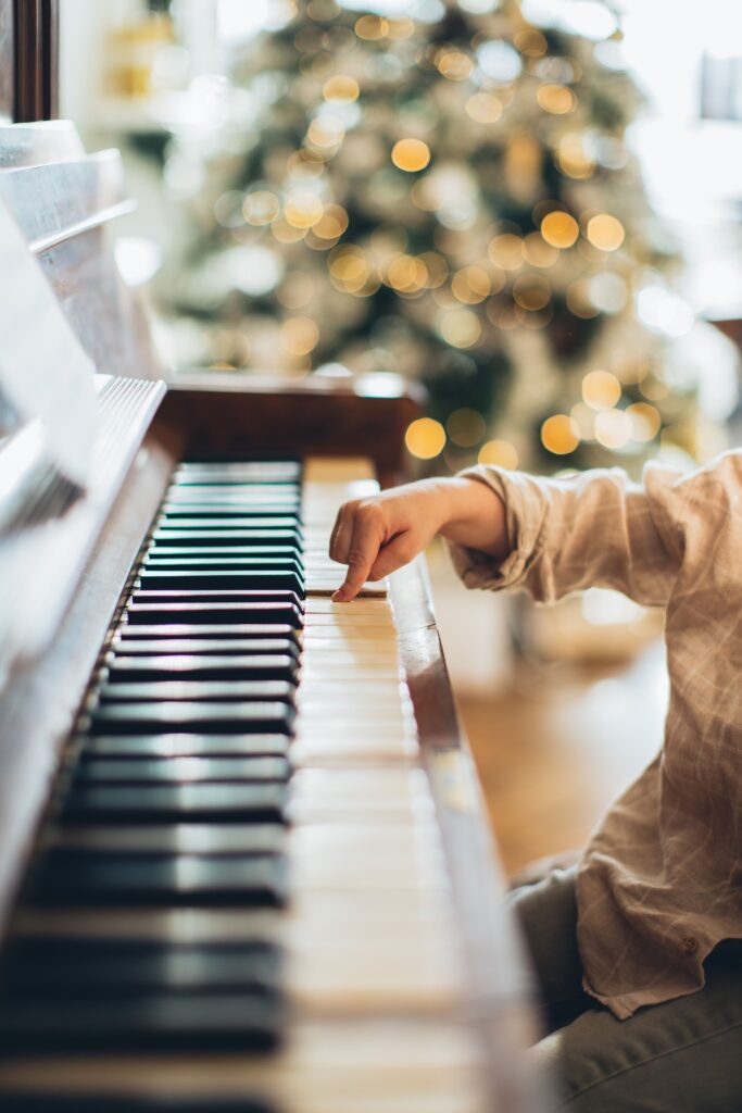 pexels-photo-5859793-5859793-1 A child's hand plays a piano with Christmas lights in the background.